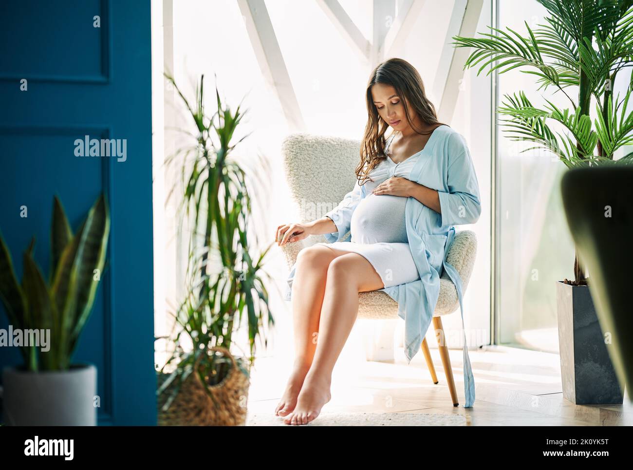 Donna felice incinta che tocca il suo appoggio della pancia sulla sedia nella casa moderna. Tenero umore foto di gravidanza sana. Foto Stock