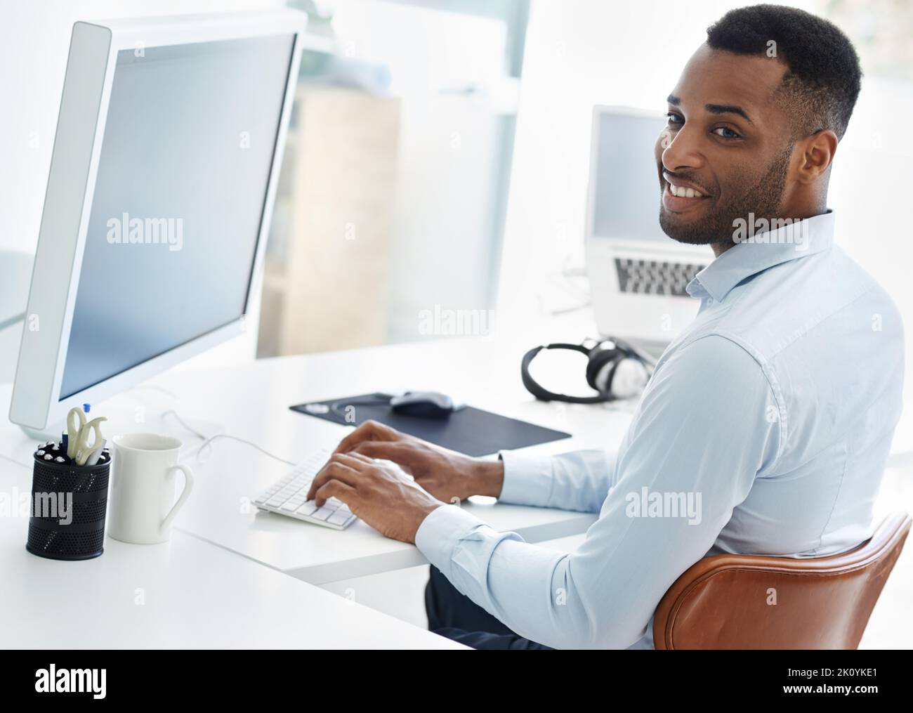 HES lavorando con un sorriso. Un bel giovane uomo d'affari afroamericano che lavora alla sua scrivania. Foto Stock