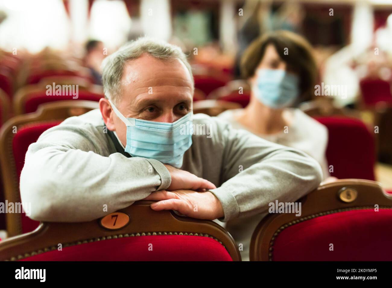 uomo maturo in maschera antivirus a teatro guardando una performance Foto Stock