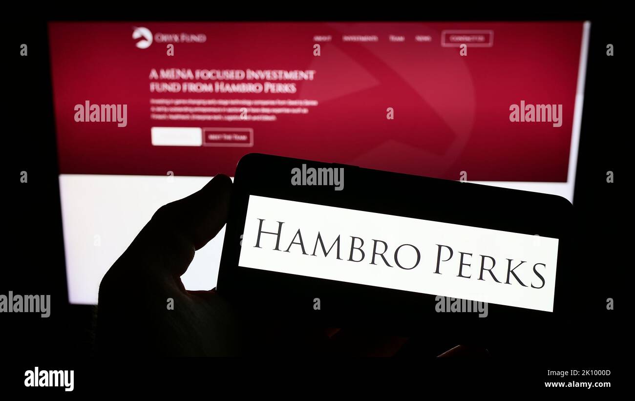 Persona in possesso di smartphone con il logo della società di investimenti britannica Hambro Perks Limited sullo schermo di fronte al sito Web. Messa a fuoco sul display del telefono. Foto Stock