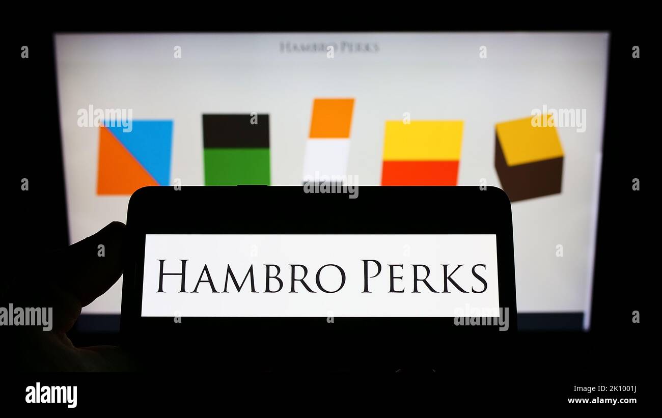 Persona che tiene il cellulare con il logo della società di investimento britannica Hambro Perks Limited sullo schermo di fronte alla pagina web. Messa a fuoco sul display del telefono. Foto Stock