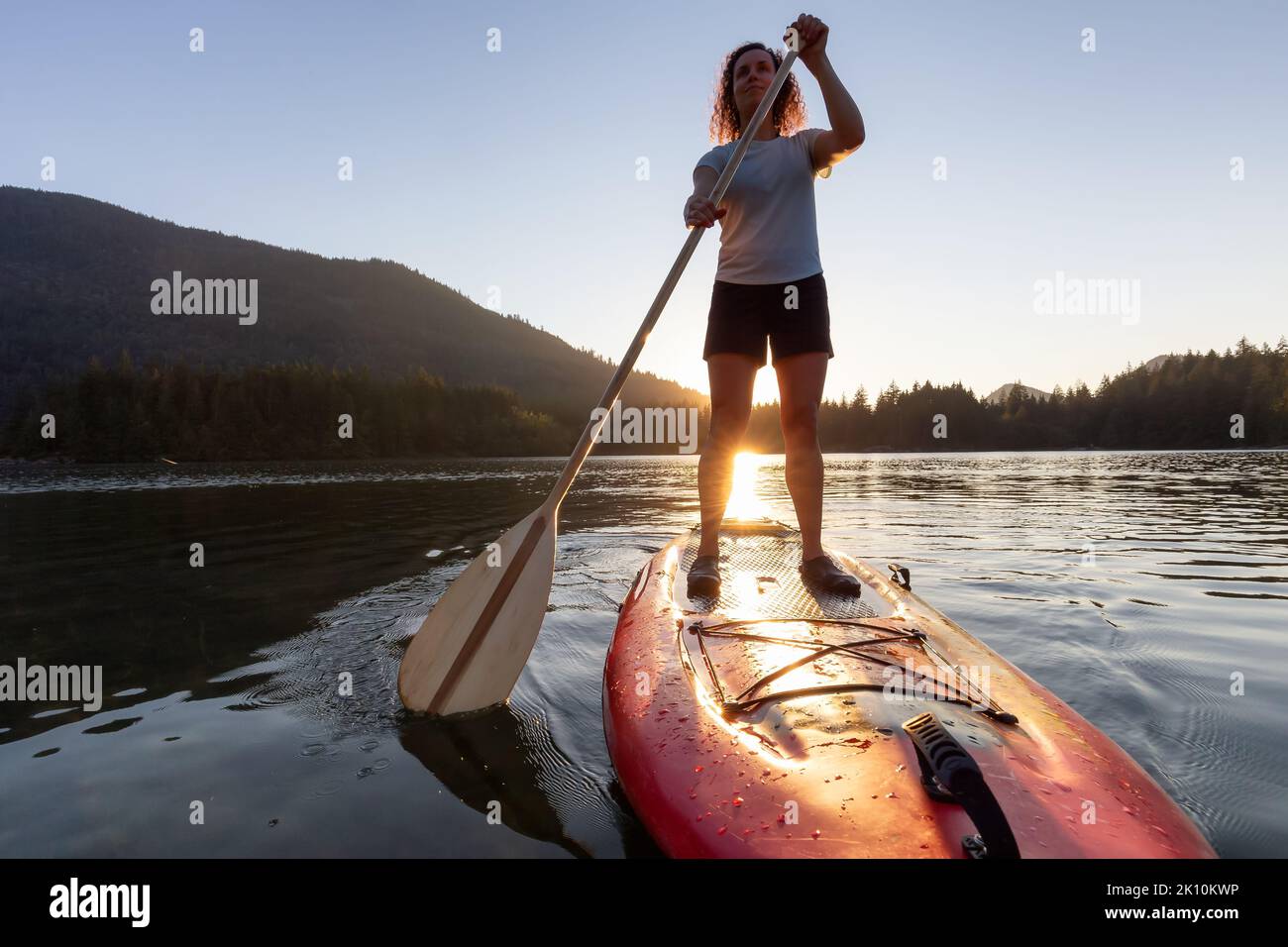 Donna avventurosa che paddling su un paddle board in un lago tranquillo. Foto Stock