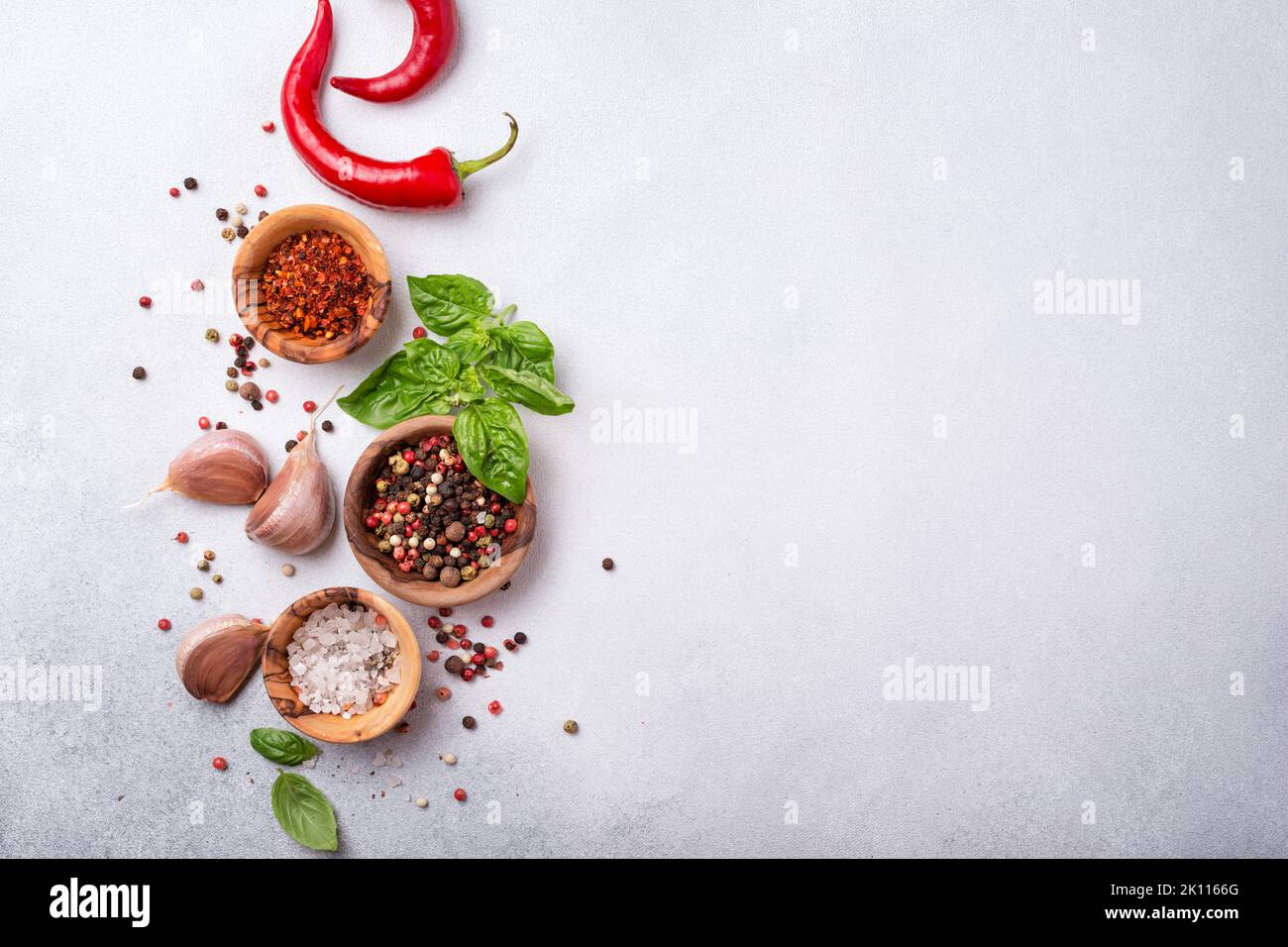 Vista dall'alto di peppercorn, sale, aglio, basilico e peperoncino rosso caldo per cibi speziati e aromatici su fondo grigio in cemento con spazio copia Foto Stock