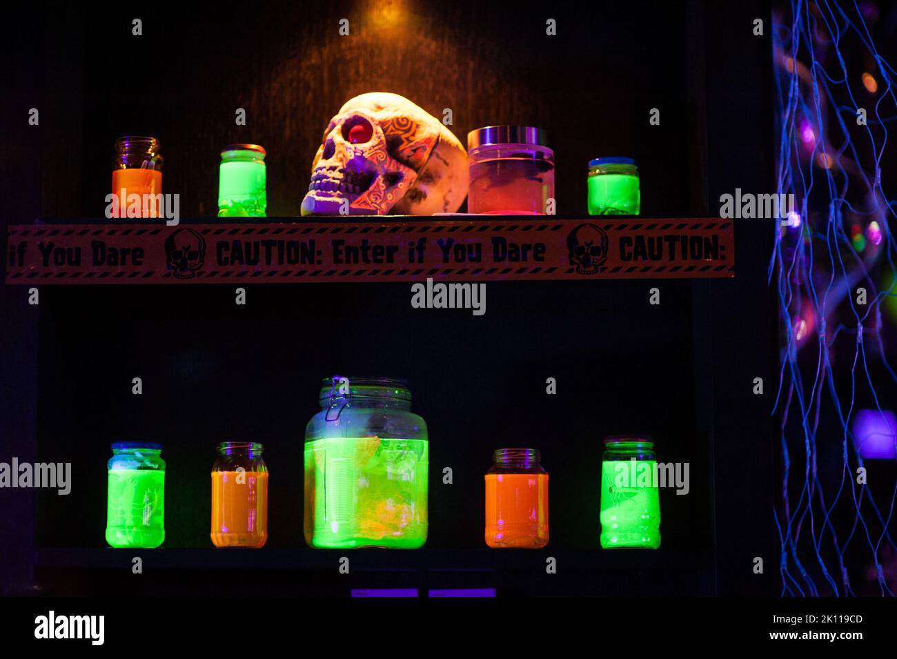 Un cranio, nastro di attenzione e vasi con liquido verde e arancione al neon sullo scaffale di un fresco, indoor Halloween party. Idee alternative di decorazione dell'anca. Foto Stock