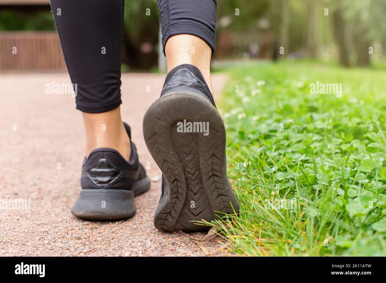gambe di donna, in sneaker nere , camminando lungo un sentiero fatto di piccola pietra rossa Foto Stock
