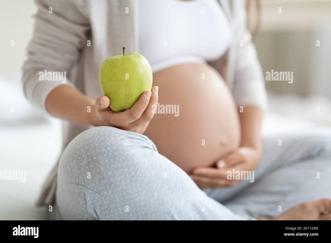 Corto di donna incinta che tiene la mela e che tocca il ventre Foto Stock