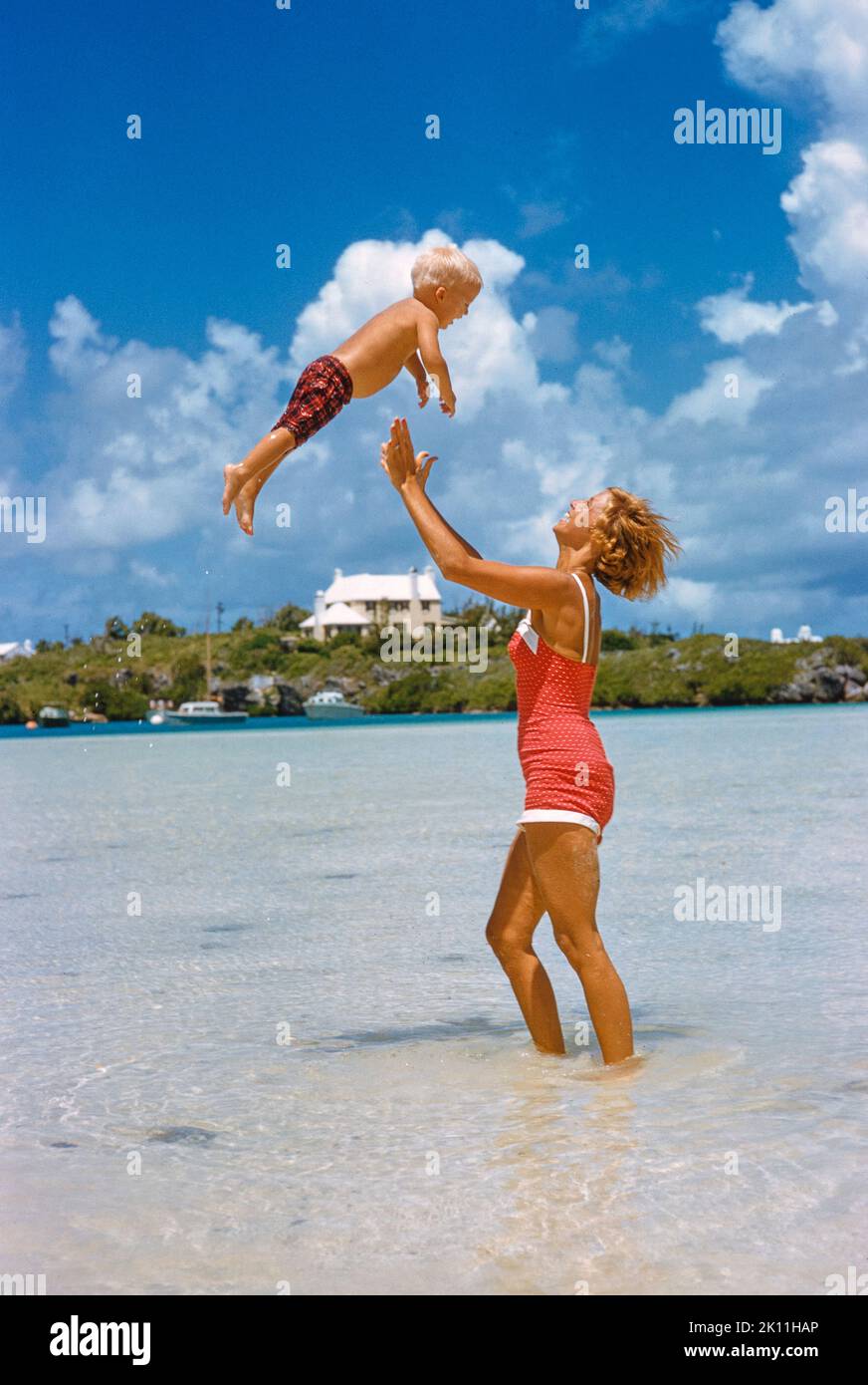 Donna che lancia giocosamente Young Boy in Air a Beach, Bermuda, toni Frissell Collection, aprile 1956 Foto Stock