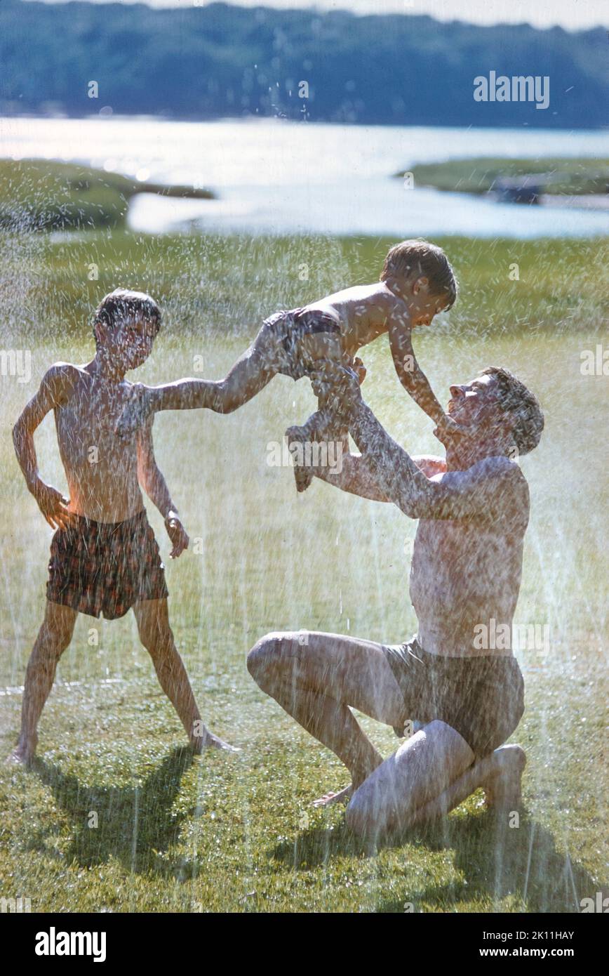 Padre che gioca con due figli vicino agli irrigatori d'acqua, toni Frissell Collection, luglio 1956 Foto Stock