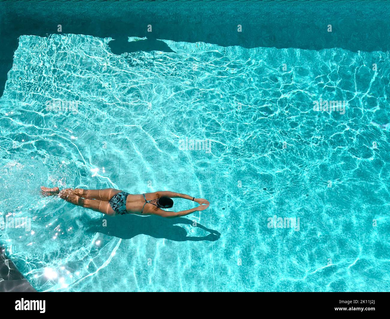 Donna che nuota a faccia in giù nella piscina all'aperto in una giornata di sole Foto Stock