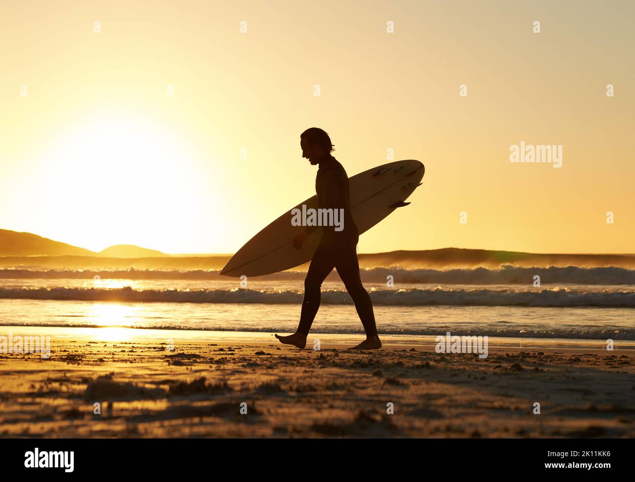 Il modo migliore per rilassarsi: Un uomo che cammina da solo con la sua tavola da surf lungo la spiaggia. Foto Stock