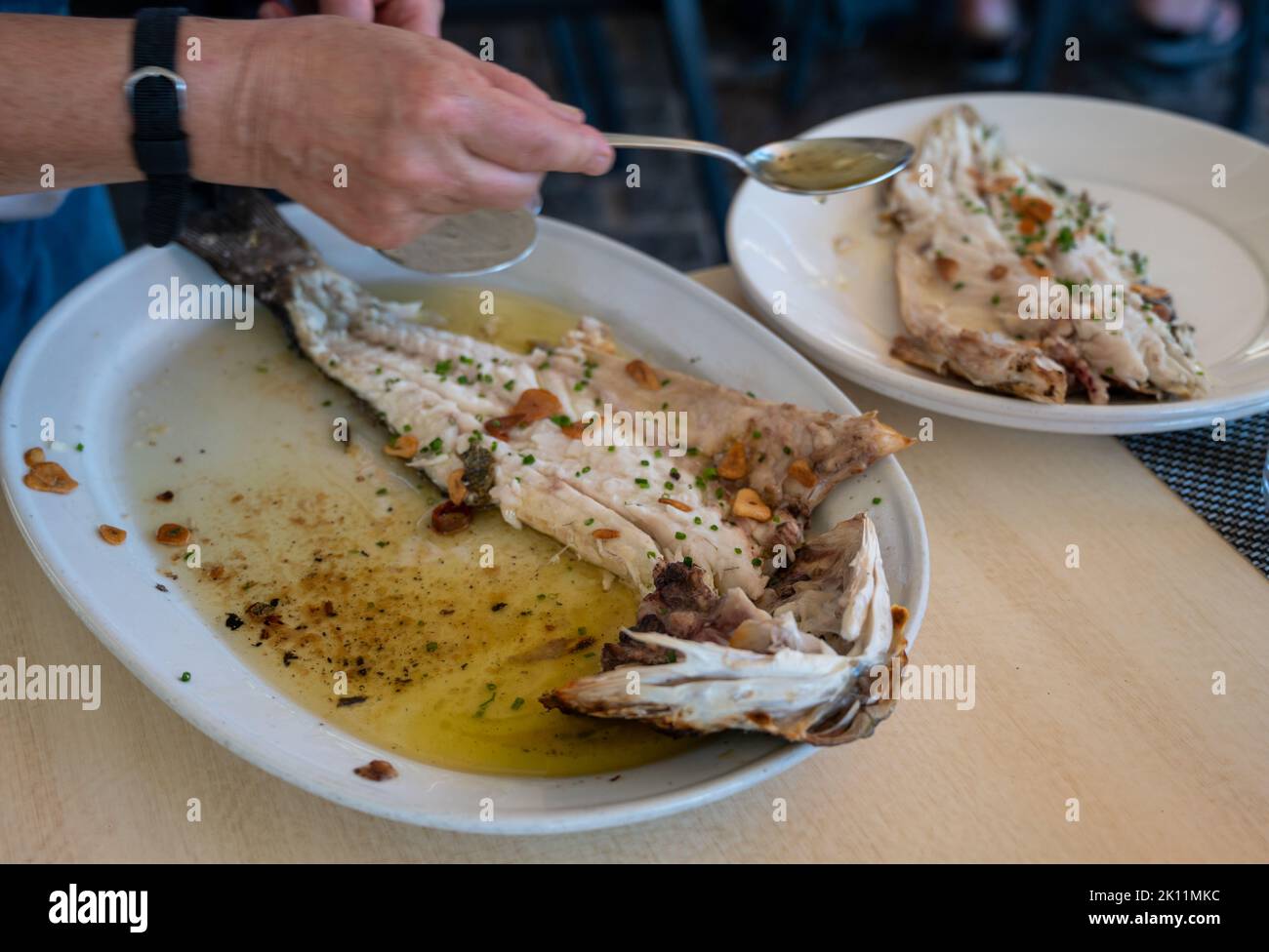 Serve in ristorante di pesce fresco alla griglia con aglio e olio d'oliva su vecchi parrillas di pesce branzino al piccolo villaggio di pescatori Getaria, basco Foto Stock