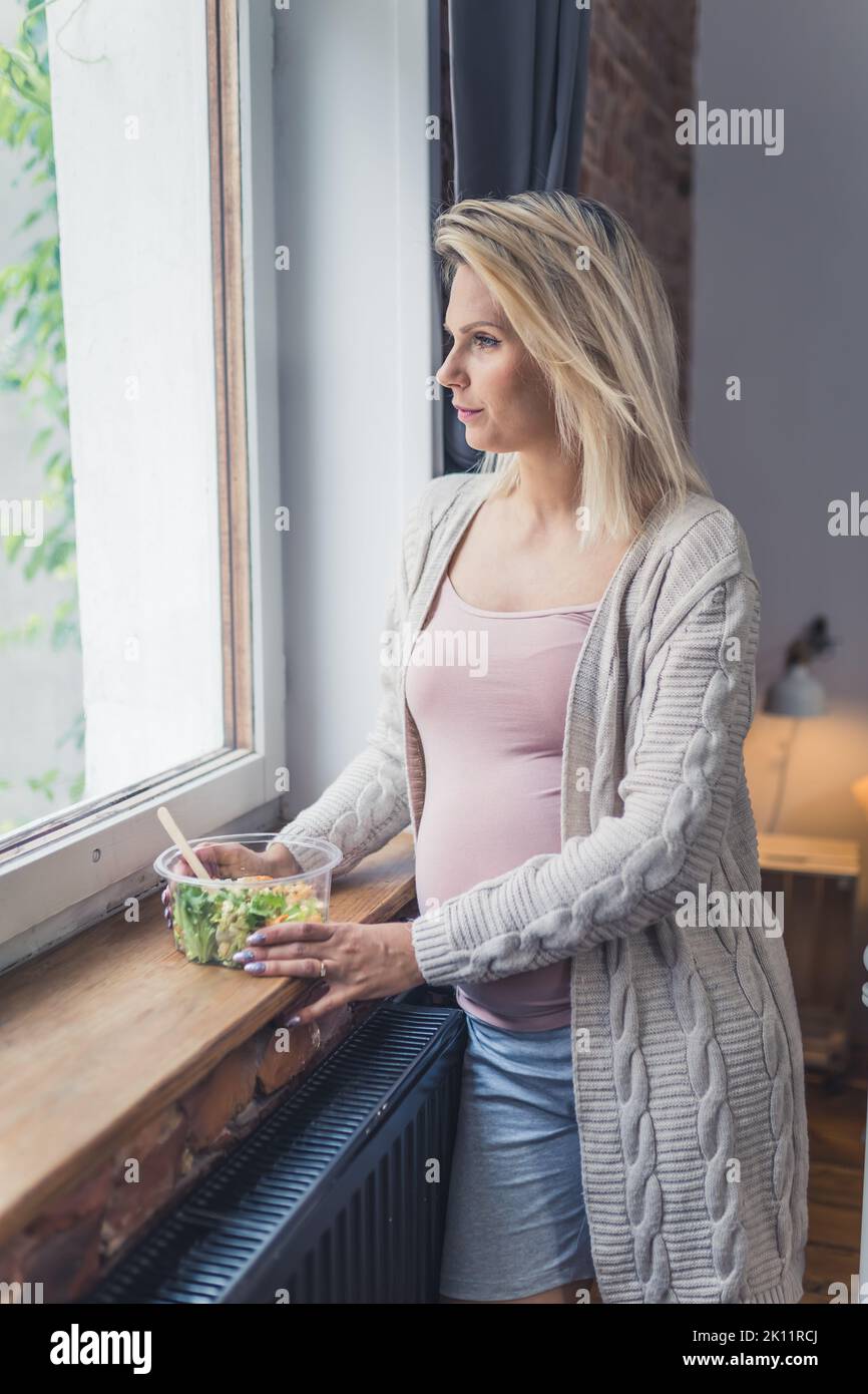 Piano di alimentazione sano durante la gravidanza. Giovane donna incinta caucasica in piedi vicino alla finestra con un nutriente, ricco di vitamine insalata pasto per la crescita di un feto sano. Foto di alta qualità Foto Stock