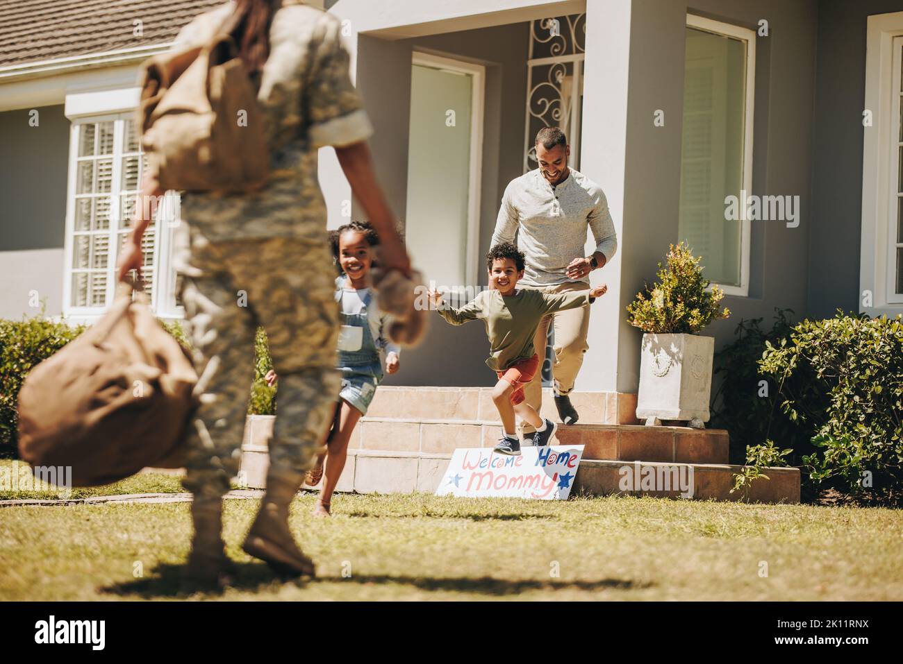 Soldato che riceve un caloroso benvenuto da suo marito e dai suoi figli. Donna militare riunitesi con la sua famiglia dopo aver servito nell'esercito. Servizio americano Foto Stock