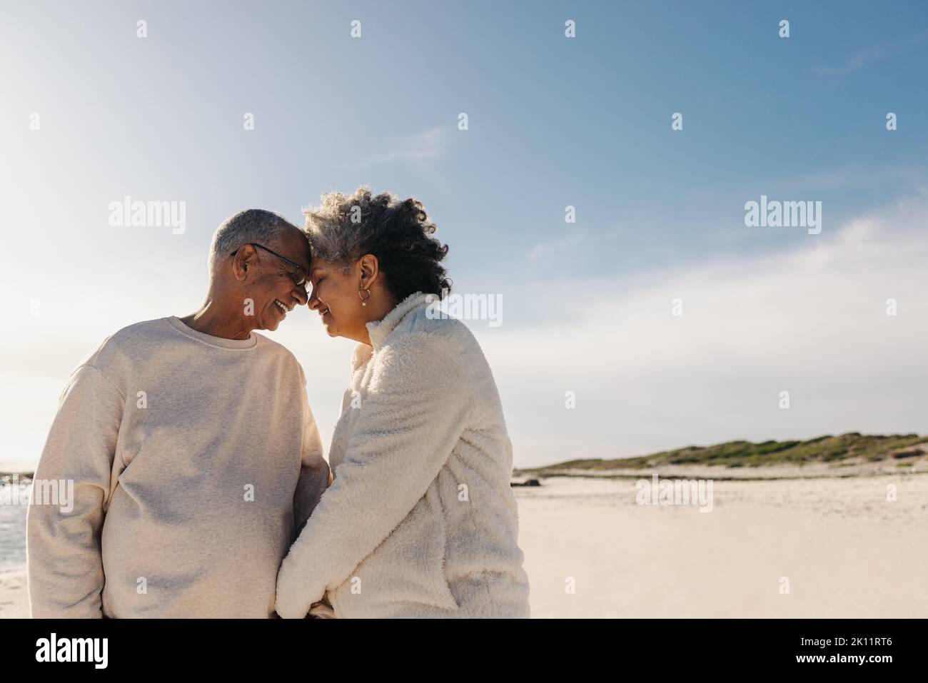 Coppia anziana affettuosa che sorride e tocca la testa insieme in spiaggia. Coppia matura che condivide un momento romantico all'aperto. Felice anziano cou Foto Stock