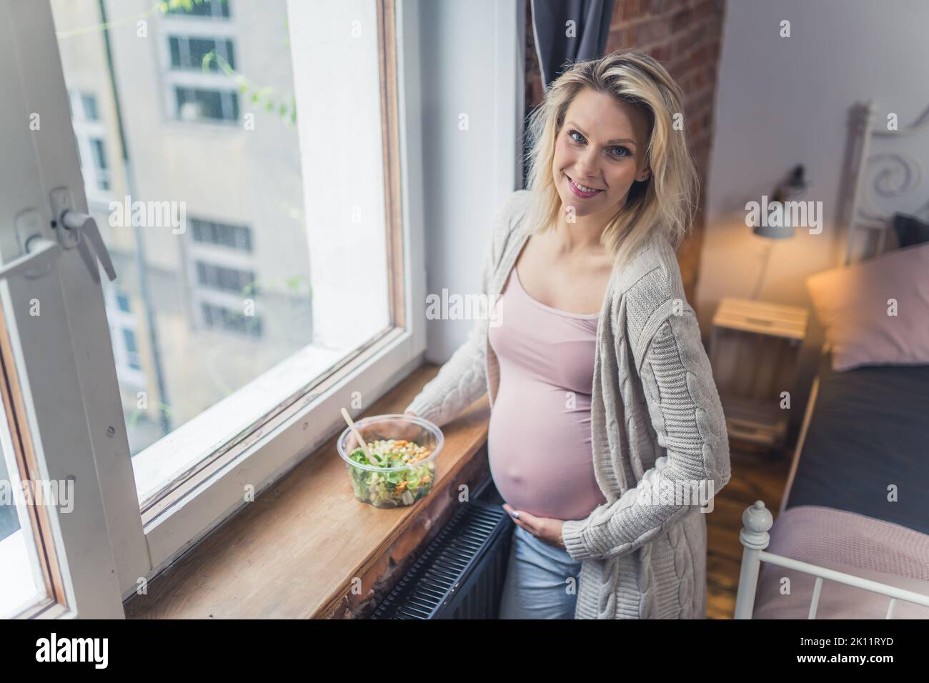 Mangiare sano durante la gravidanza. Giovane donna incinta caucasica in piedi vicino alla finestra con un nutriente, ricco di vitamine insalata pasto per la crescita di un feto sano. Foto di alta qualità Foto Stock