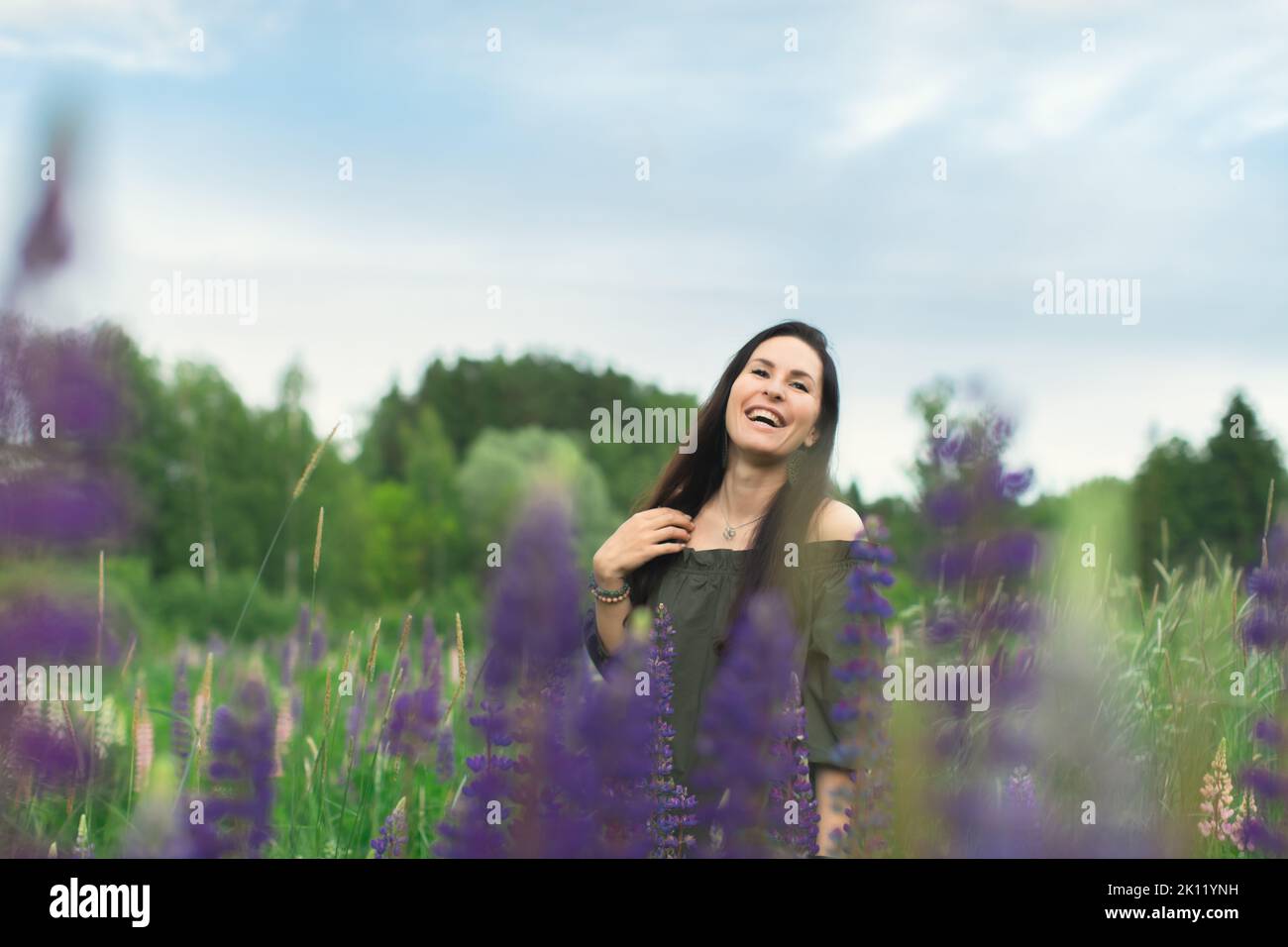 Una donna attraente in un campo con un bouquet estivo di fiori selvatici Lupinus. Vista frontale. Foto Stock