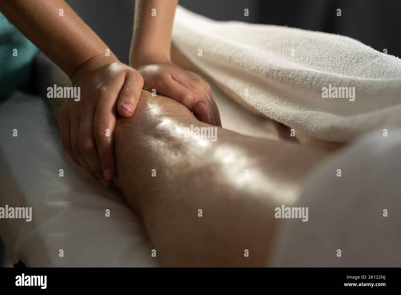 Massaggio sportivo. Fisioterapista femminile che massaggia le gambe di un giovane atleta maschile. Mani da massaggiatore in primo piano che fanno massaggio ai piedi. Foto Stock