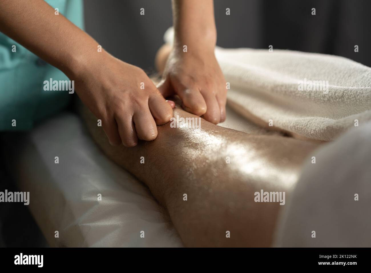 Massaggio sportivo. Fisioterapista femminile che massaggia le gambe di un giovane atleta maschile. Mani da massaggiatore in primo piano che fanno massaggio ai piedi. Foto Stock