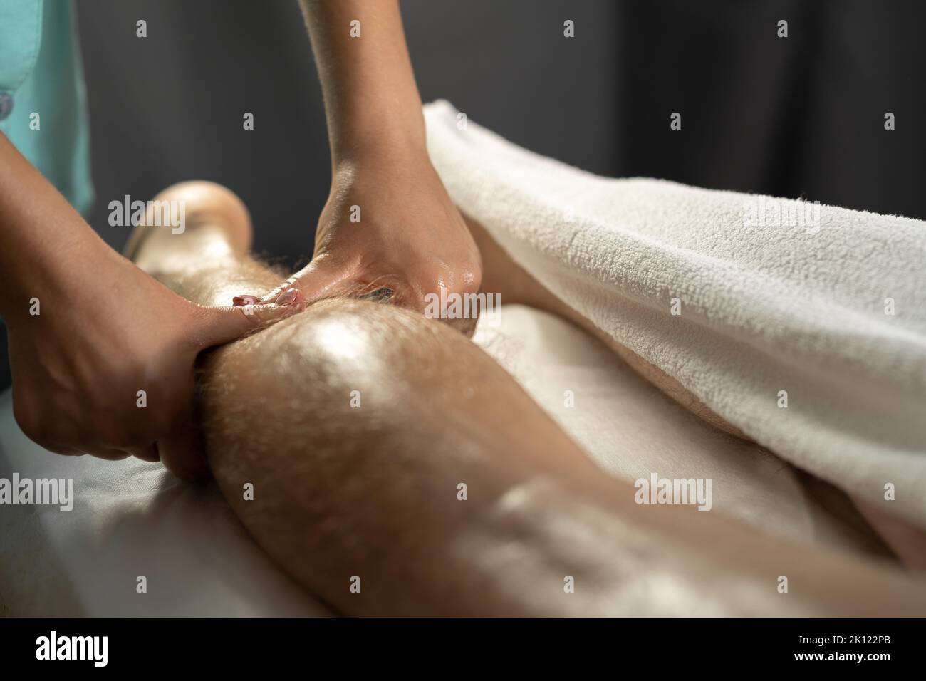 Terapista femminile che dà massaggio alle gambe e ai polpacci al paziente atleta sul letto in clinica. Massaggio sportivo. Una massaggiatrice che lavora con un paziente massaggia il suo Foto Stock