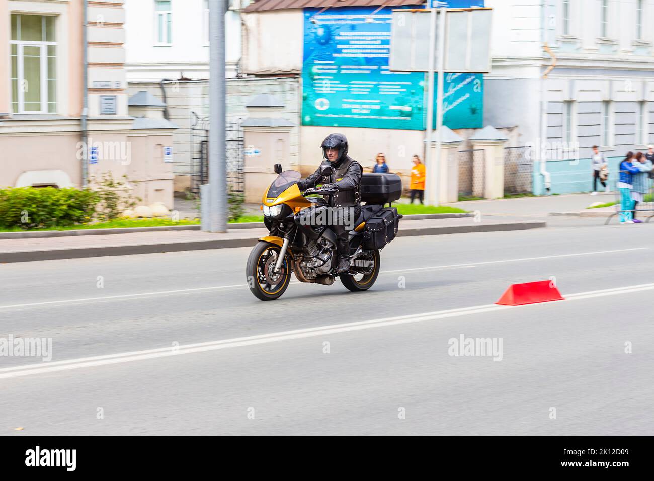 Un attraente uomo adulto in uniforme pelle nera in sella oro moto veloce attraverso la città oltre gli edifici sulla città strada Tomsk Russia 10 agosto 2022 Foto Stock
