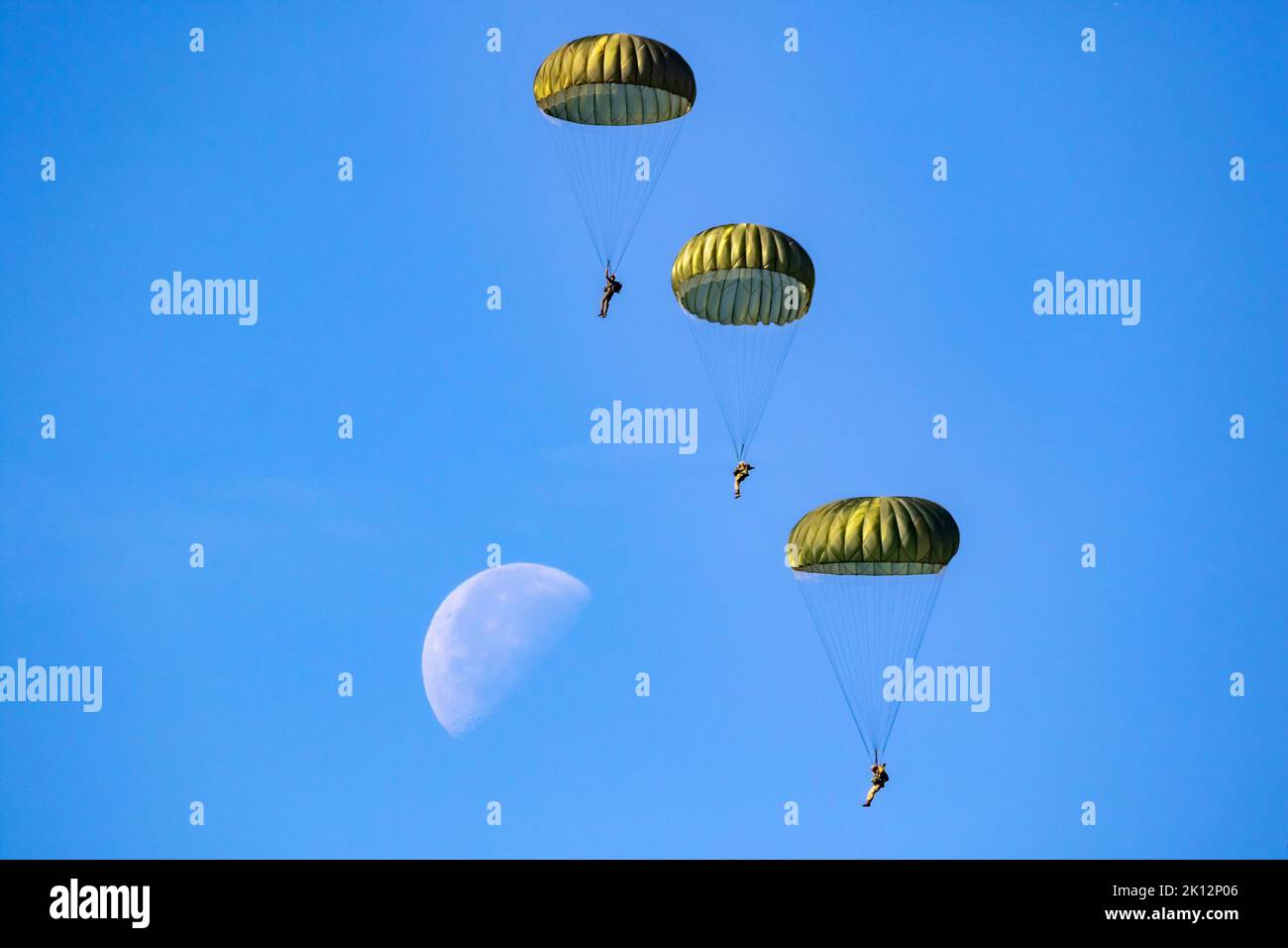 Paracadutisti militari paracadutisti che saltano fuori da un aereo di forza in una giornata di cielo blu chiaro con la luna. Foto Stock