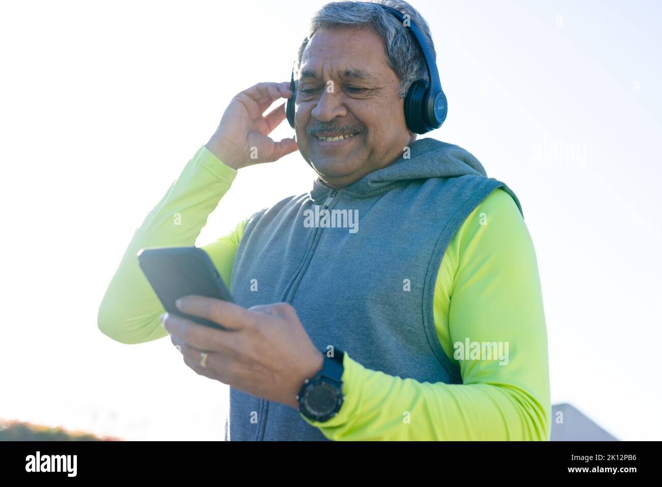 Sorridente uomo biraciale anziano in abiti sportivi e cuffie con smartphone Foto Stock