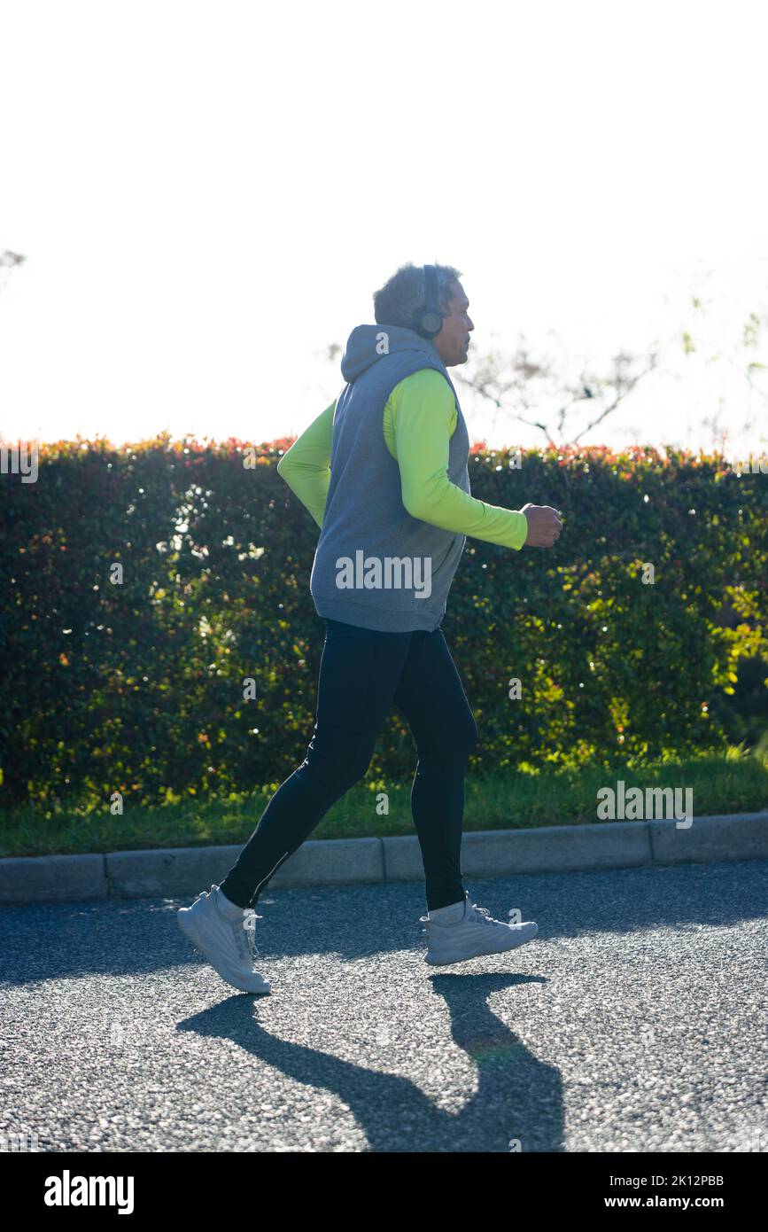 Immagine verticale dell'uomo anziano biraciale in abiti sportivi e cuffie per jogging su strada Foto Stock