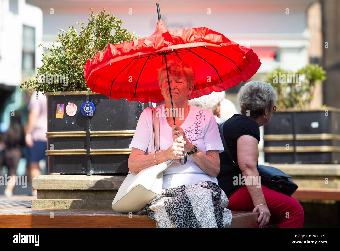 Una donna con una unbrella rossa si rifugia dal sole mentre la gente nella città di York, North Yorkshire sopporta la giornata più calda del record come il temperato Foto Stock