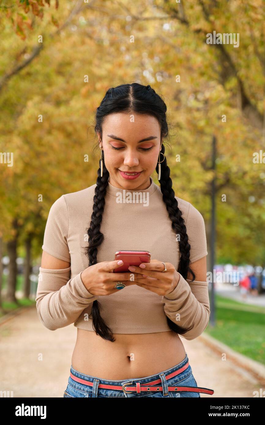 Giovane ragazza latina sorridente utilizzando lo smartphone per strada. Foto Stock