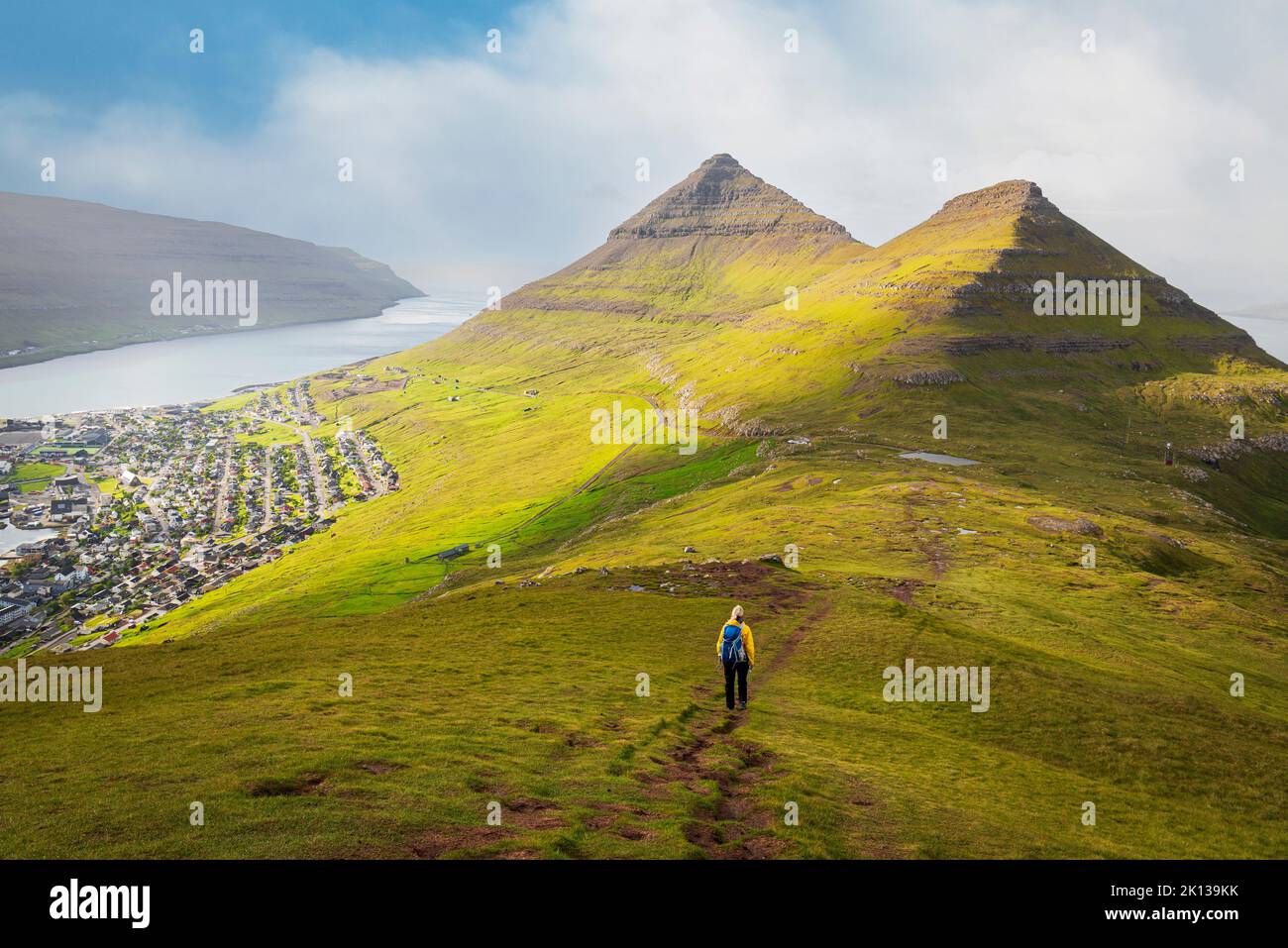 Escursionista con giacca gialla cammina lungo il monte Klakker, Klaksvik, Borooy Island, Faroe Islands, Danimarca, Europa Foto Stock