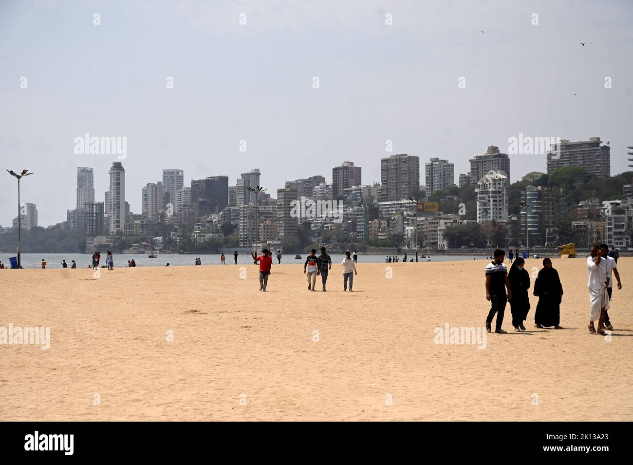 Persone tra cui musulmani a passeggiare sulla spiaggia di Juhu, alti edifici cittadini sullo sfondo, Mumbai, India, Asia Foto Stock