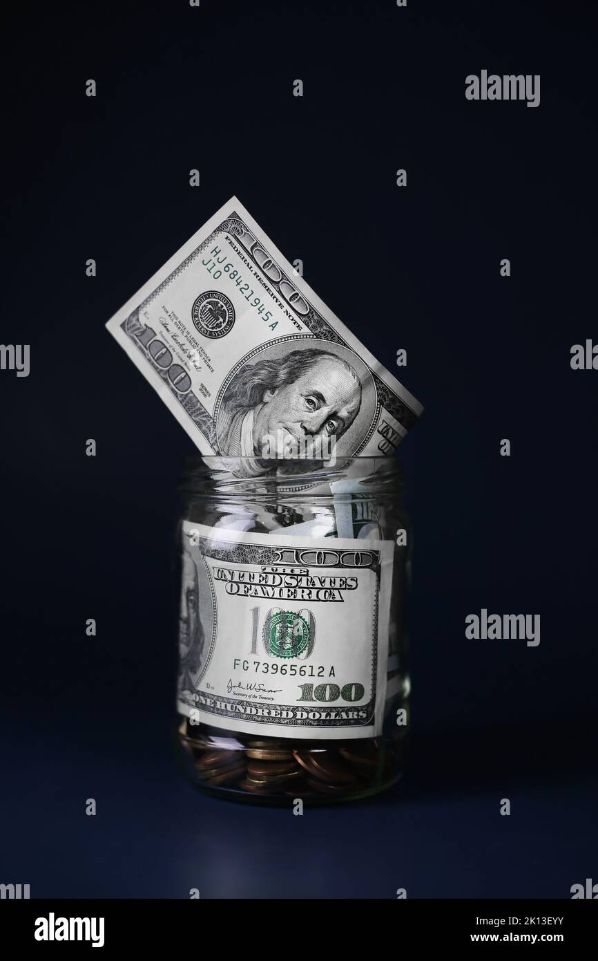 Dollari in un vaso di vetro con monete su uno sfondo blu scuro. Concetto di risparmio economico Foto Stock