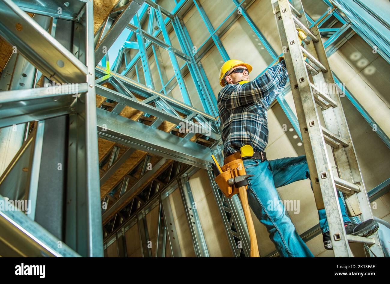 Contraente caucasico arrampicarsi su una scala all'interno della struttura della Camera d'acciaio durante il suo lavoro di sviluppo. Nuovo edificio commerciale. Foto Stock