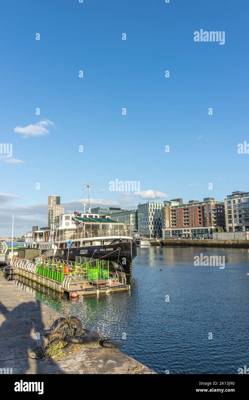 La MV Cill Airne barca sul fiume Liffey, con moderni appartamenti e uffici dietro, Dublino, Irlanda. Foto Stock