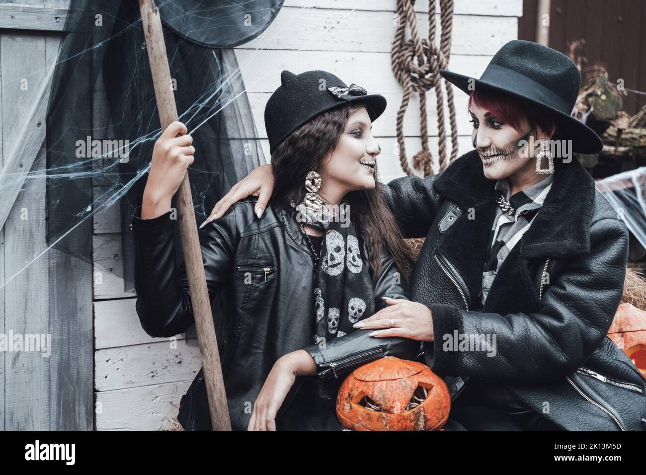 Famiglia spaventosa, madre, figlia che celebra Halloween. Fienile di strada. Zucca jack-o-lantern.terrificante nero cranio mezza faccia trucco e costumi strega, br Foto Stock