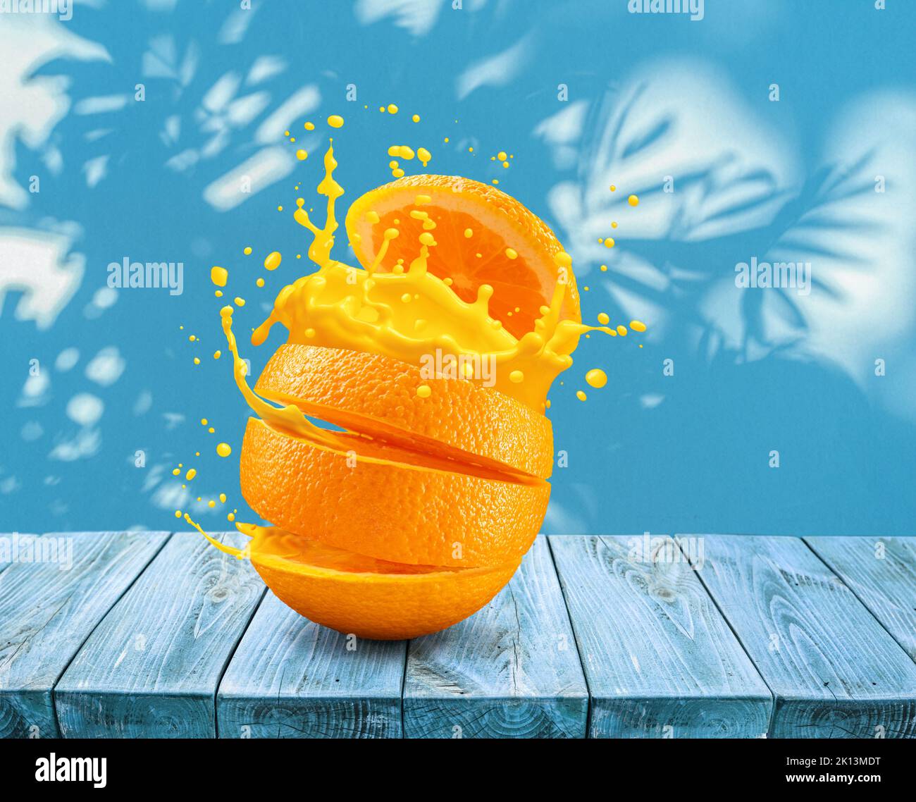 Frutta d'arancia tagliata a fette spruzzando sul succo d'arancia sul tavolo e sulla parete blu con le ombre delle foglie sullo sfondo. Foto Stock