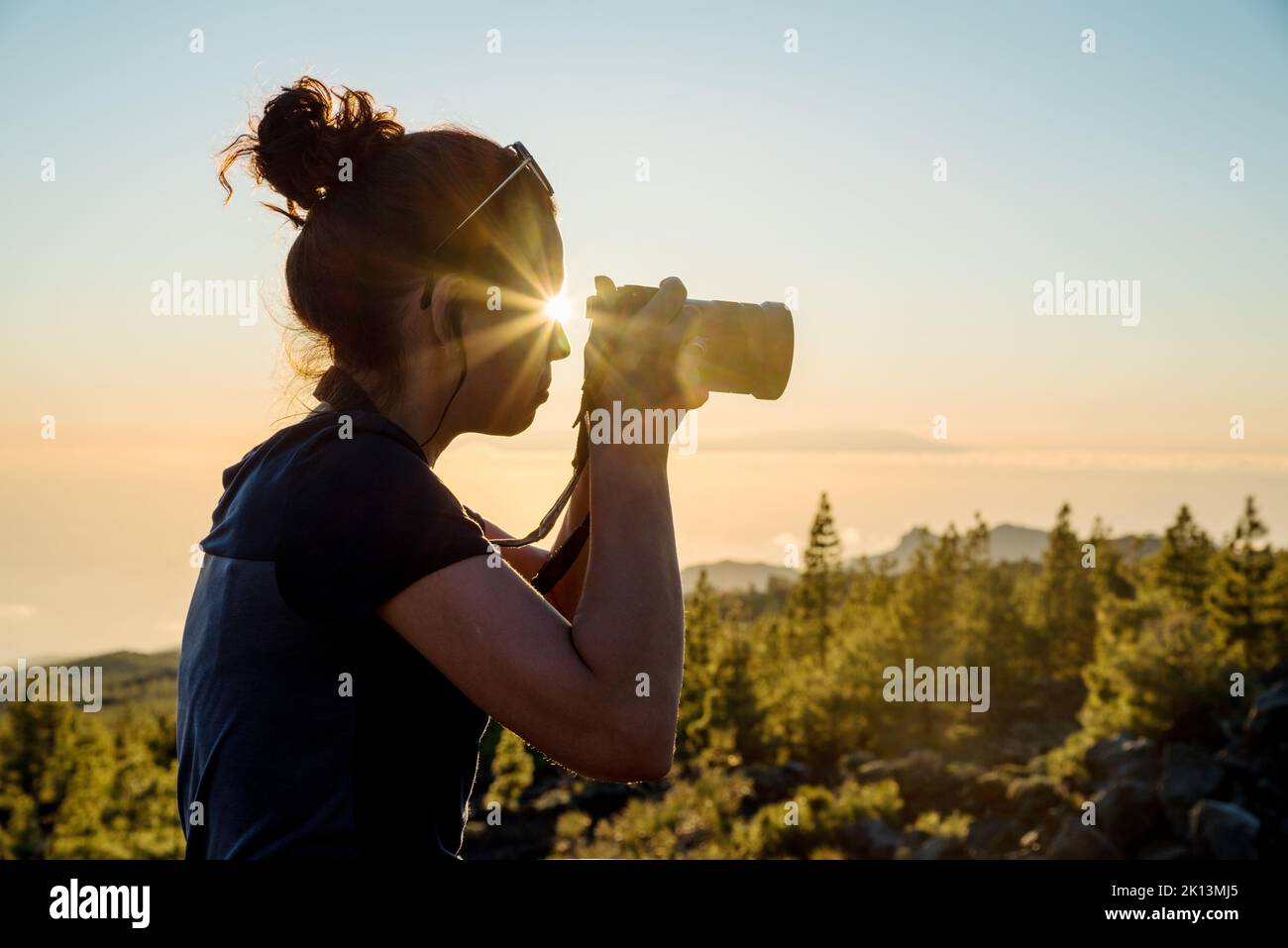 Silhouette di donna con fotocamera. Donna scatta foto dell'isola di la Gomera ai raggi del sole che tramonta. Isola di Tenerife. Foto Stock
