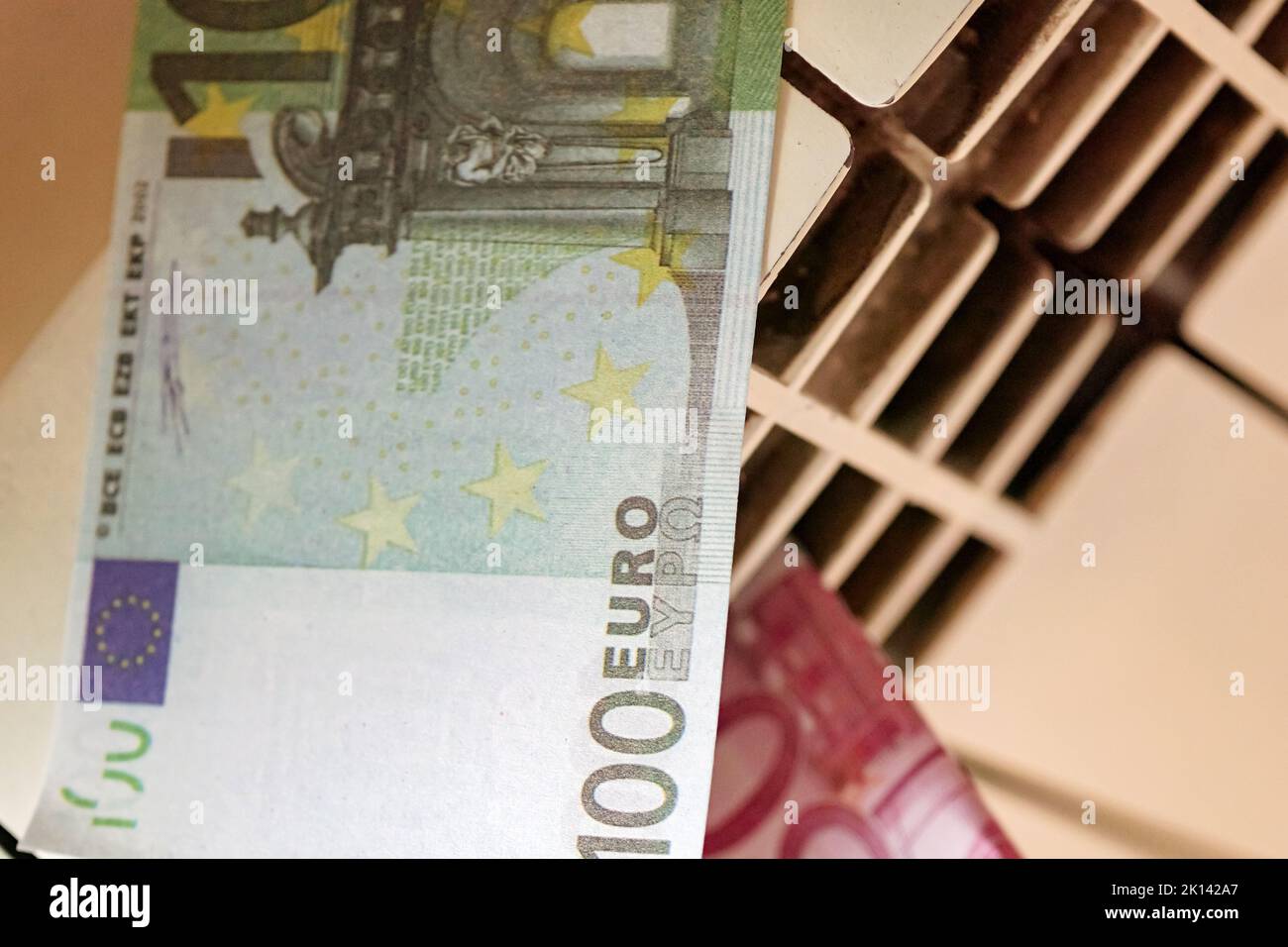 Banconote in euro in un radiatore di riscaldamento centrale, il concetto di costi di riscaldamento costosi in crisi energetica Foto Stock