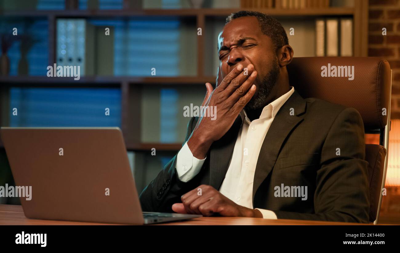 Stanco sonnolento manager maschile a scrivere sul notebook funziona in ufficio di notte che soffre di privazione del sonno sensazione di stanchezza a causa di overwork sonnolenza infelice Foto Stock