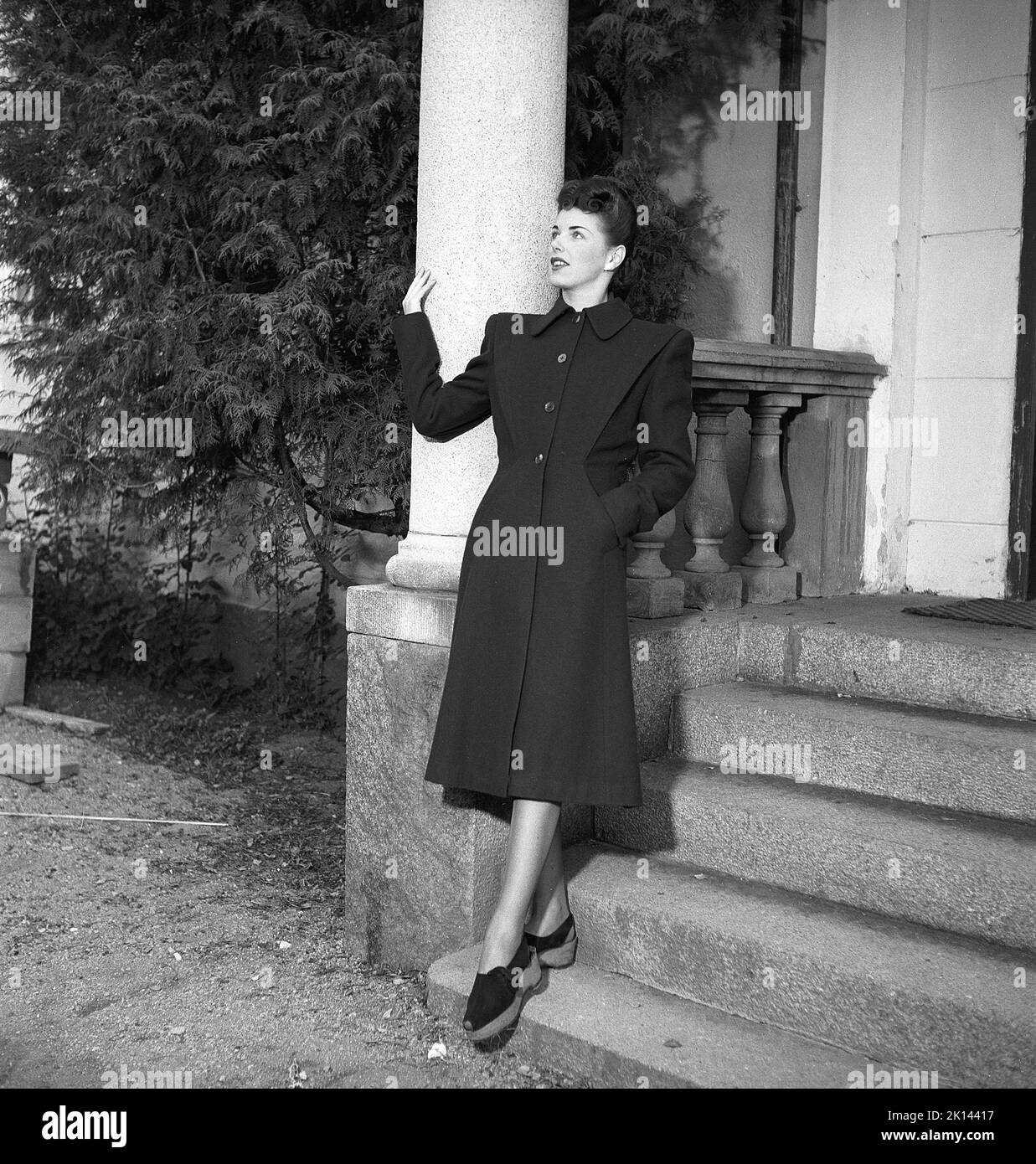 Moda femminile negli anni '1940s. Una giovane donna fotografata per una rivista femminile per mostrare la moda femminile del 1945. Il modello femminile indossa un lungo cappotto nero in tessuto scuro con bottoni solo sulla parte superiore. La sua acconciatura è molto tipica degli anni '1940s. Svezia 1945. Kristoffersson Rif. R5-3 Foto Stock