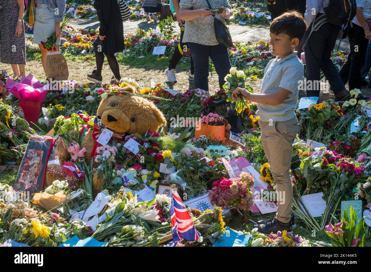 Un ragazzino mette un mazzo di fiori in memoria della defunto Regina Elisabetta II a Green Park, Londra, dove migliaia di visitatori hanno lutto la morte della Regina hanno lasciato grandi quantità di fiori e tributi floreali Foto Stock