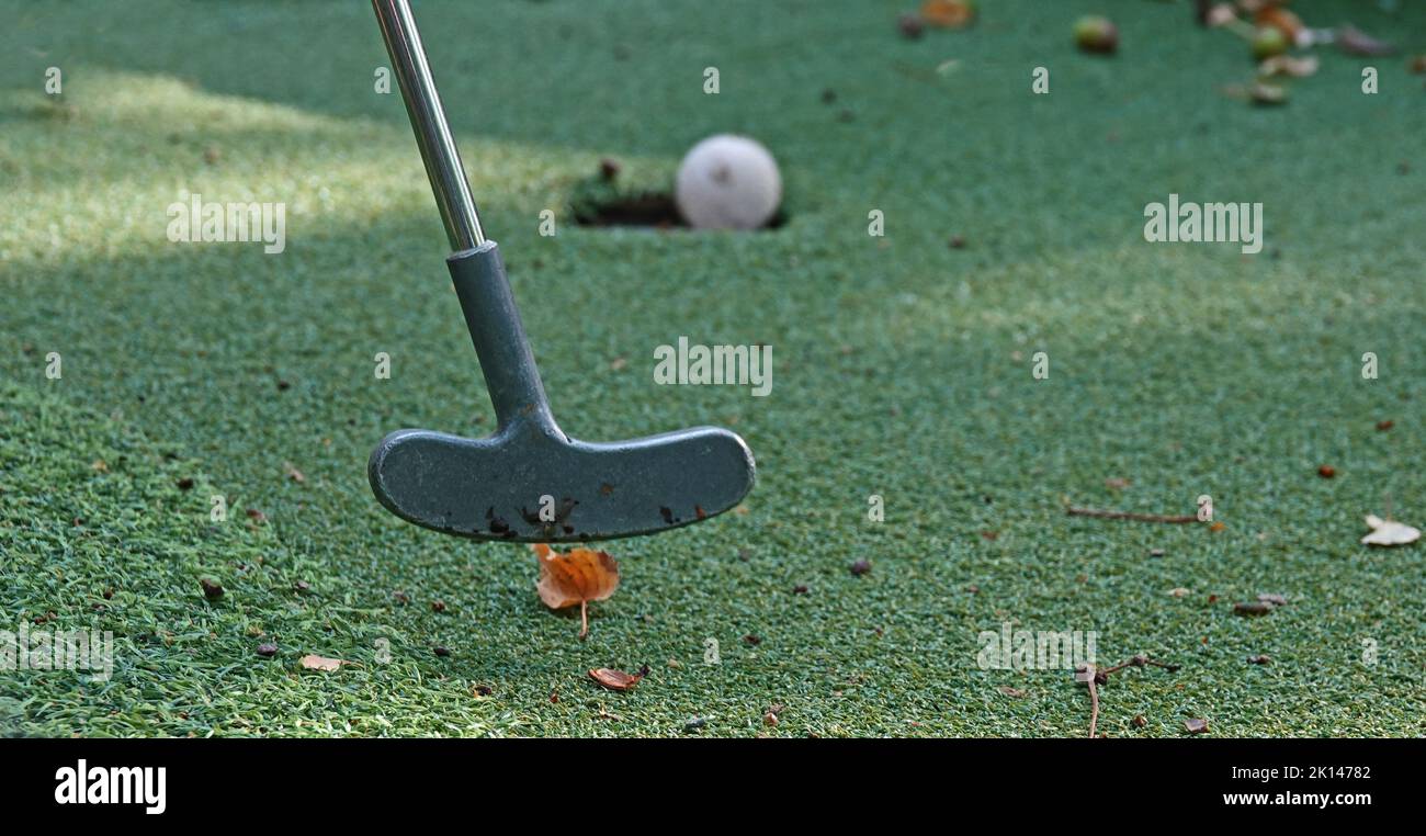 Il club ha appena colpito la palla durante un mini gioco di golf. La sfera rotola nel foro Foto Stock