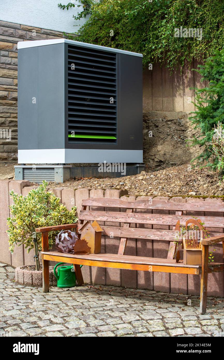 Pompa di calore moderna, pompa di calore aria-acqua nel giardino anteriore di Una casa di famiglia, di fronte ad esso Una panca fatta di legno Foto Stock