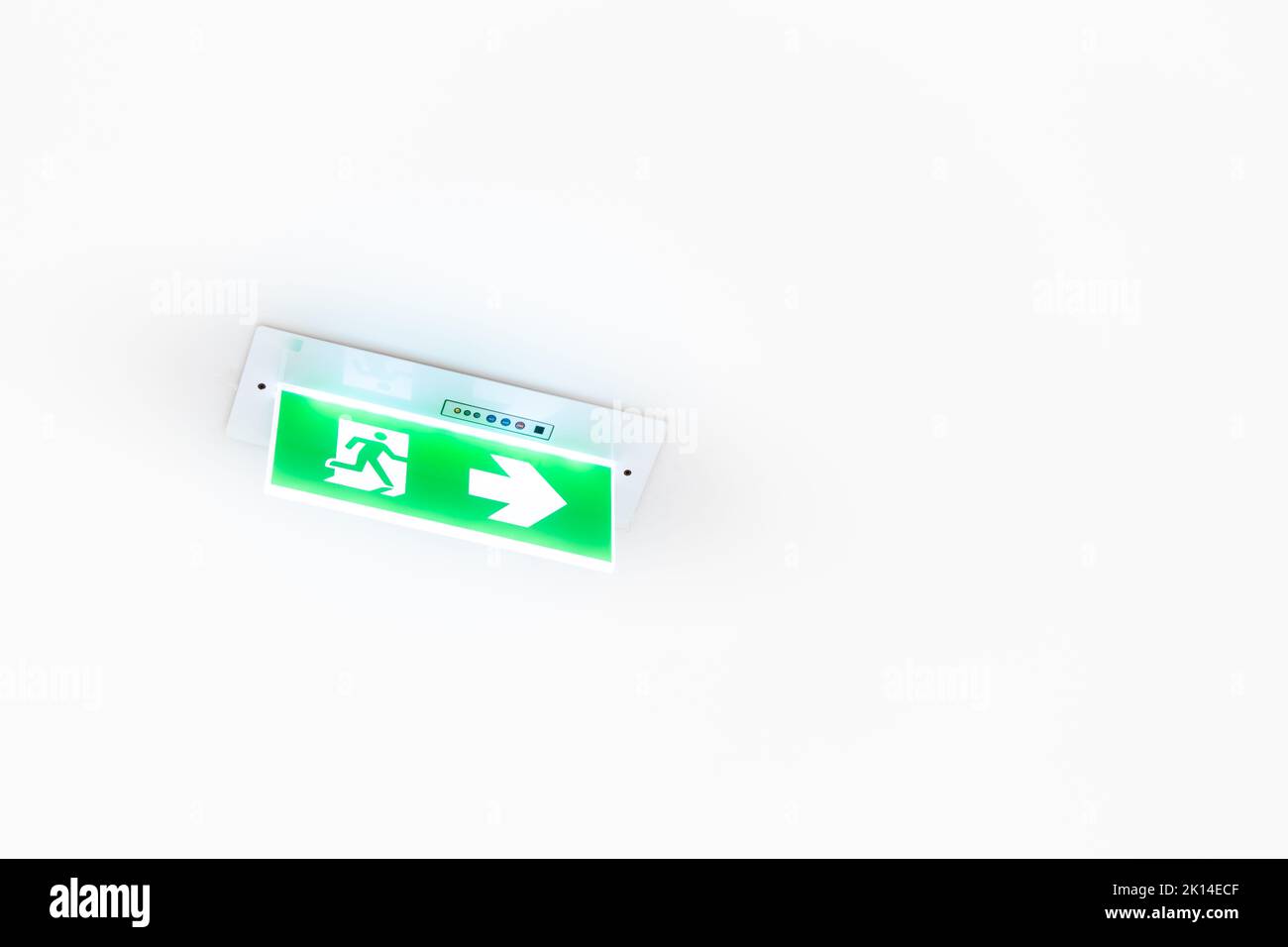 Un cartello al neon bianco raffigurante un'uscita antincendio con sfondo verde è appeso al soffitto. Foto Stock