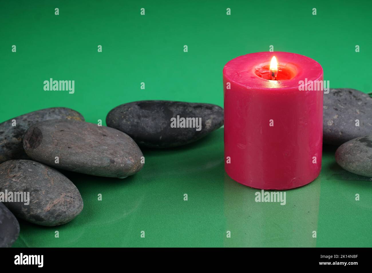 Una candela rossa che brucia accanto alle rocce con su una superficie verde Foto Stock