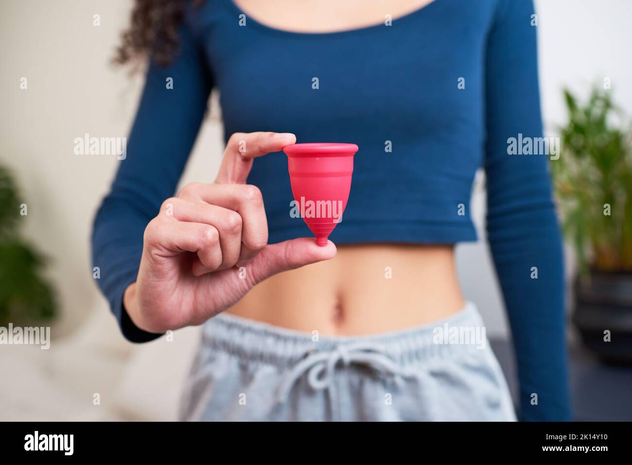 Primo piano della giovane donna che tiene la tazza mestruale mentre in pigiama Foto Stock