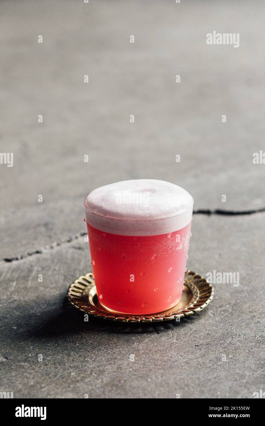Cocktail Pink Gin fizz su montagne russe in ottone su pavimento in cemento Foto Stock
