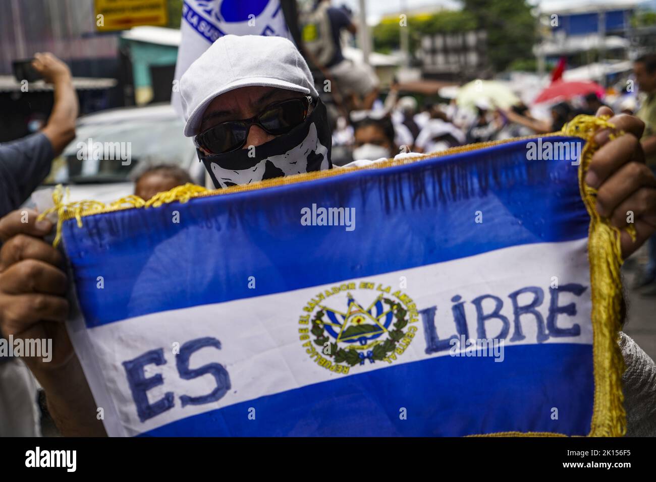 San Salvador, El Salvador. 15th Set, 2022. El Salvador 'è libero,' legge una bandiera di El Salvador tenuto in alto da un dimostratore incappucciati durante una protesta contro lo stato di emergenza. Il giorno dell'Indipendenza nel paese centroamericano, numerose persone sono scese in strada contro lo stato di emergenza che è in vigore da sei mesi. Credit: Camilo Freedman/dpa/Alamy Live News Foto Stock