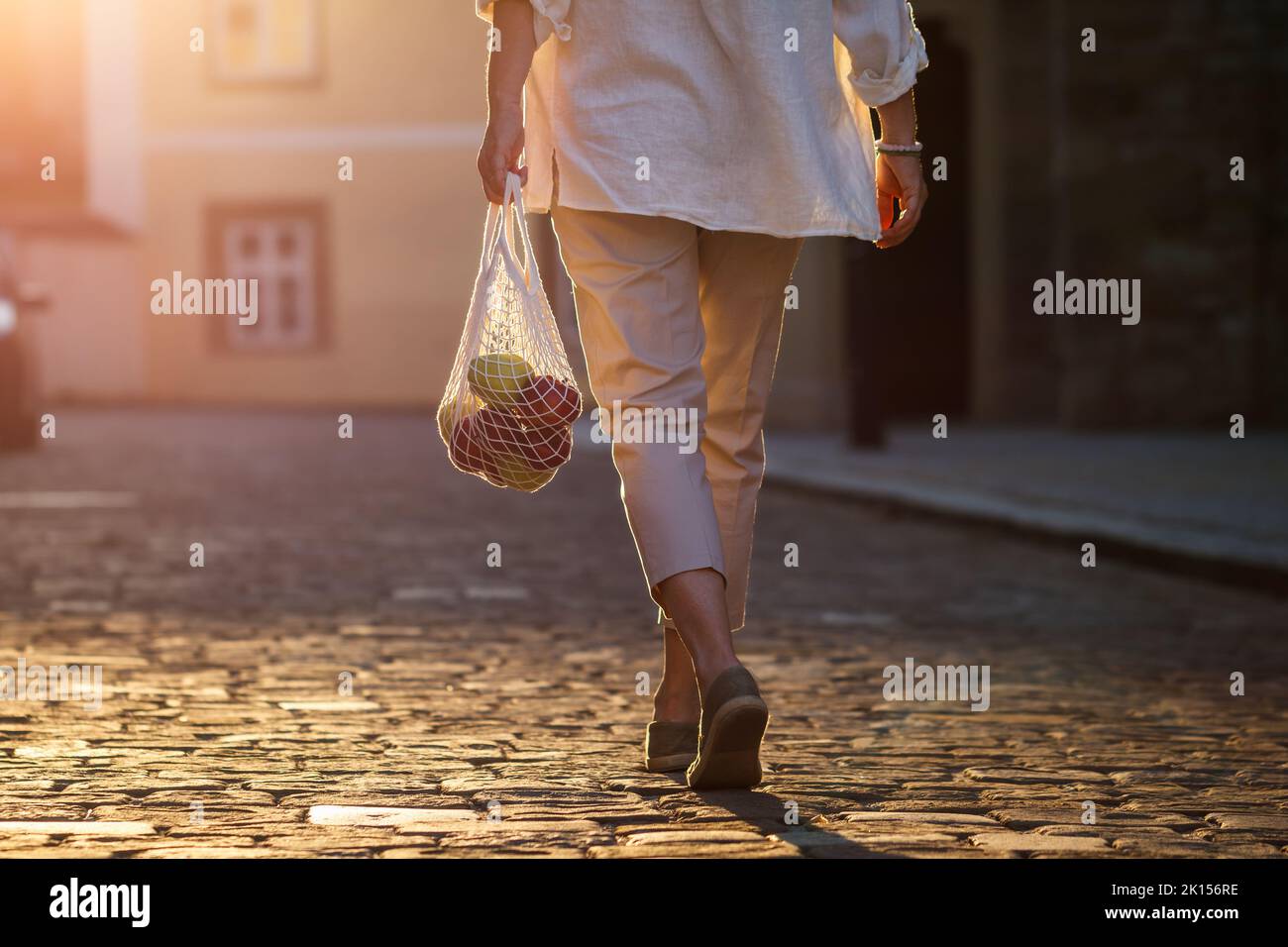 Donna cammina per strada e porta una borsa in maglia riutilizzabile dopo lo shopping. Vita cittadina Foto Stock