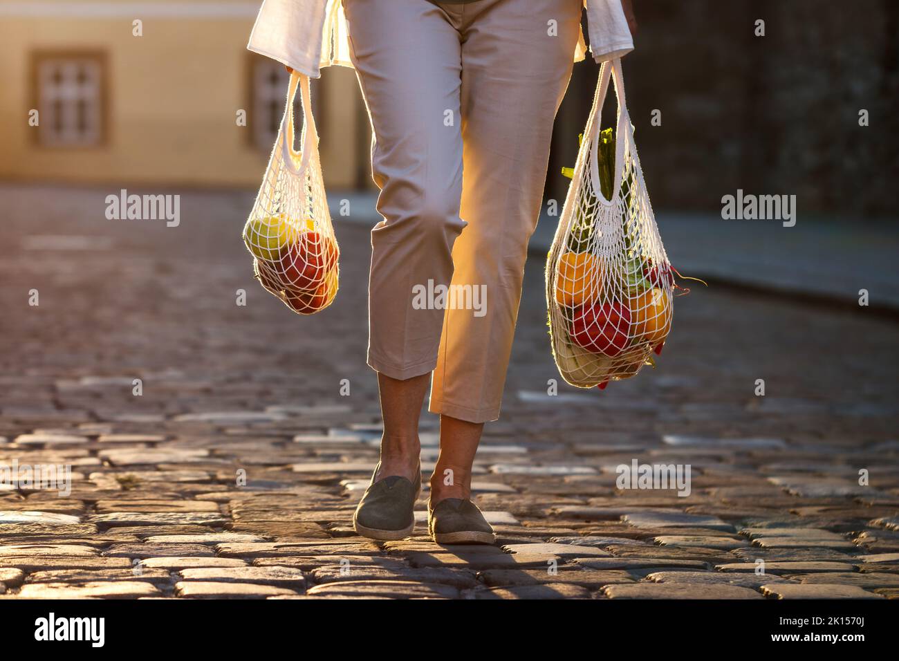 Donna cammina per strada e porta una borsa in maglia riutilizzabile dopo lo shopping. Concetto di stile di vita sostenibile e zero sprechi Foto Stock